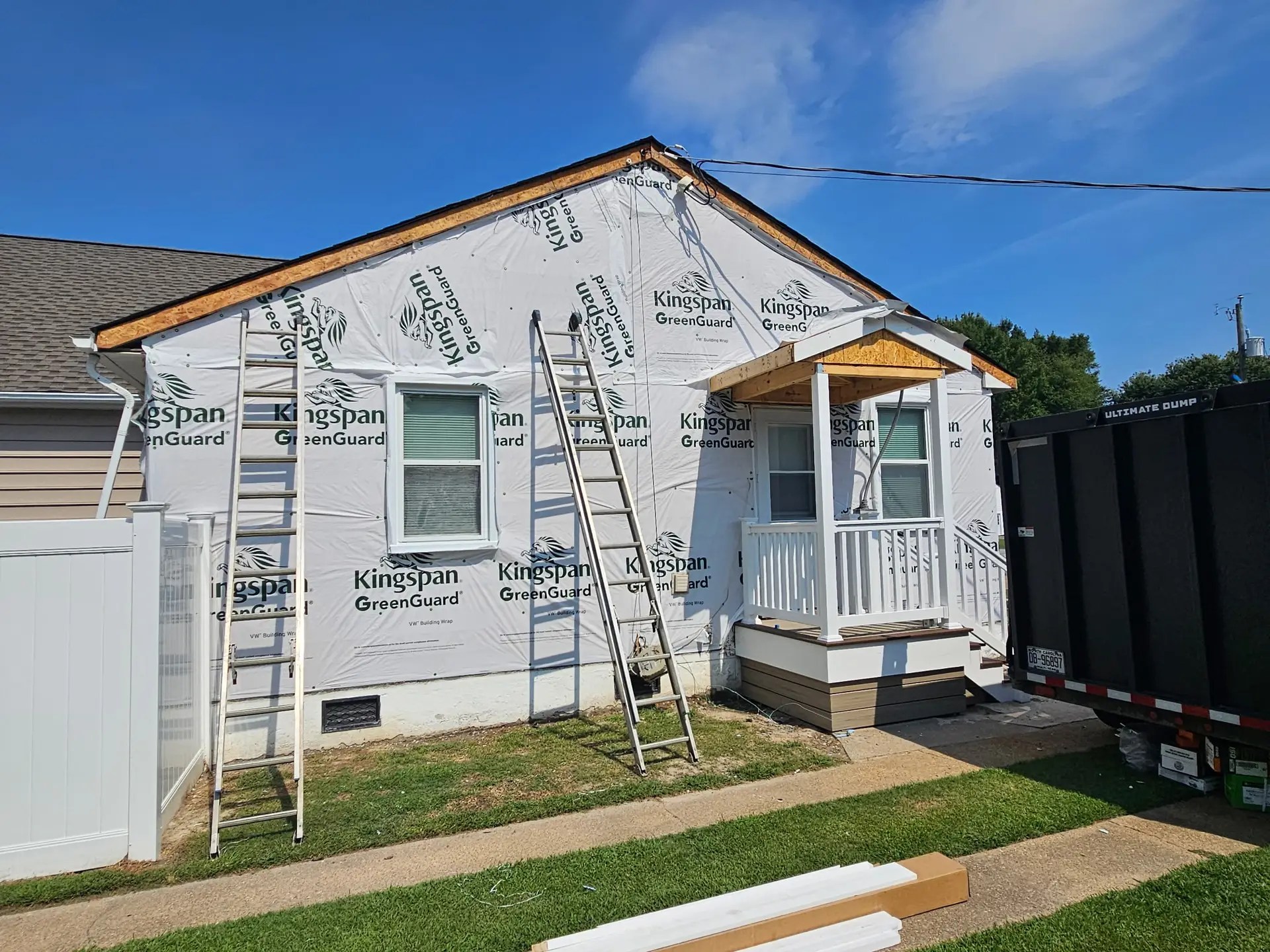 Front gable and porch of the Poquoson home with exposed house wrap and ladders during siding replacement.