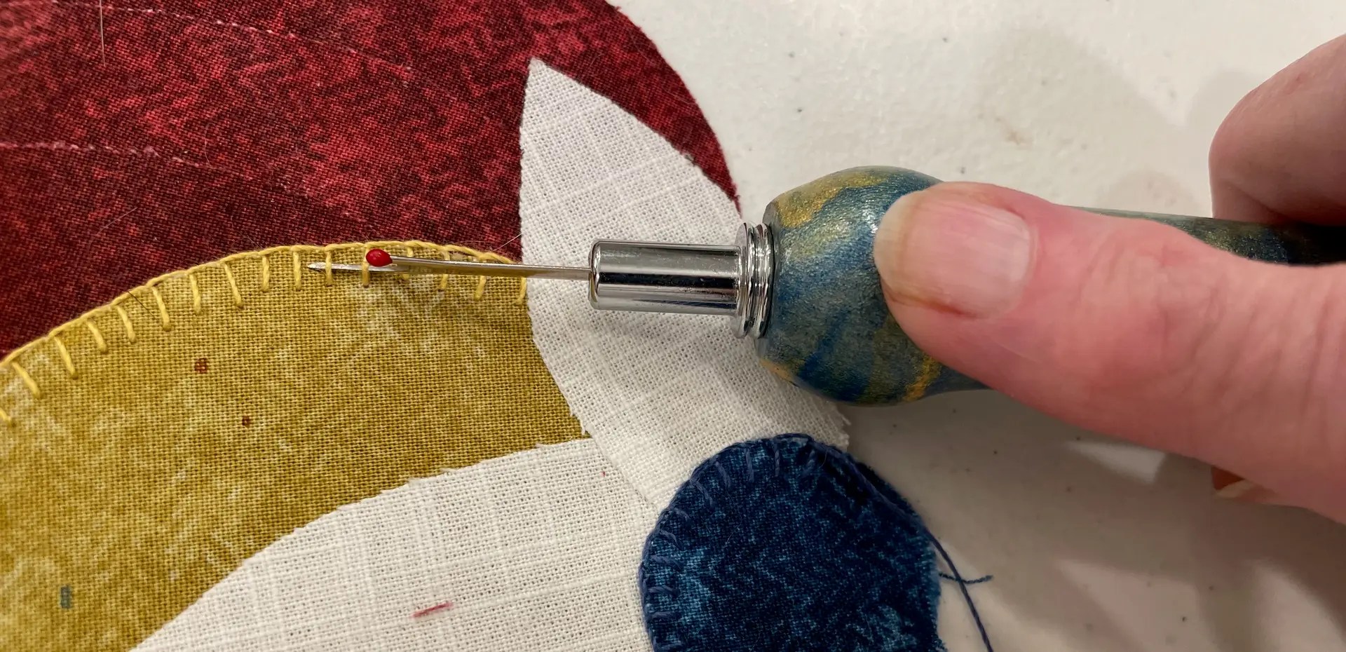 Close-up of a hand using a seam ripper to remove stitches from a gold fabric appliqué.