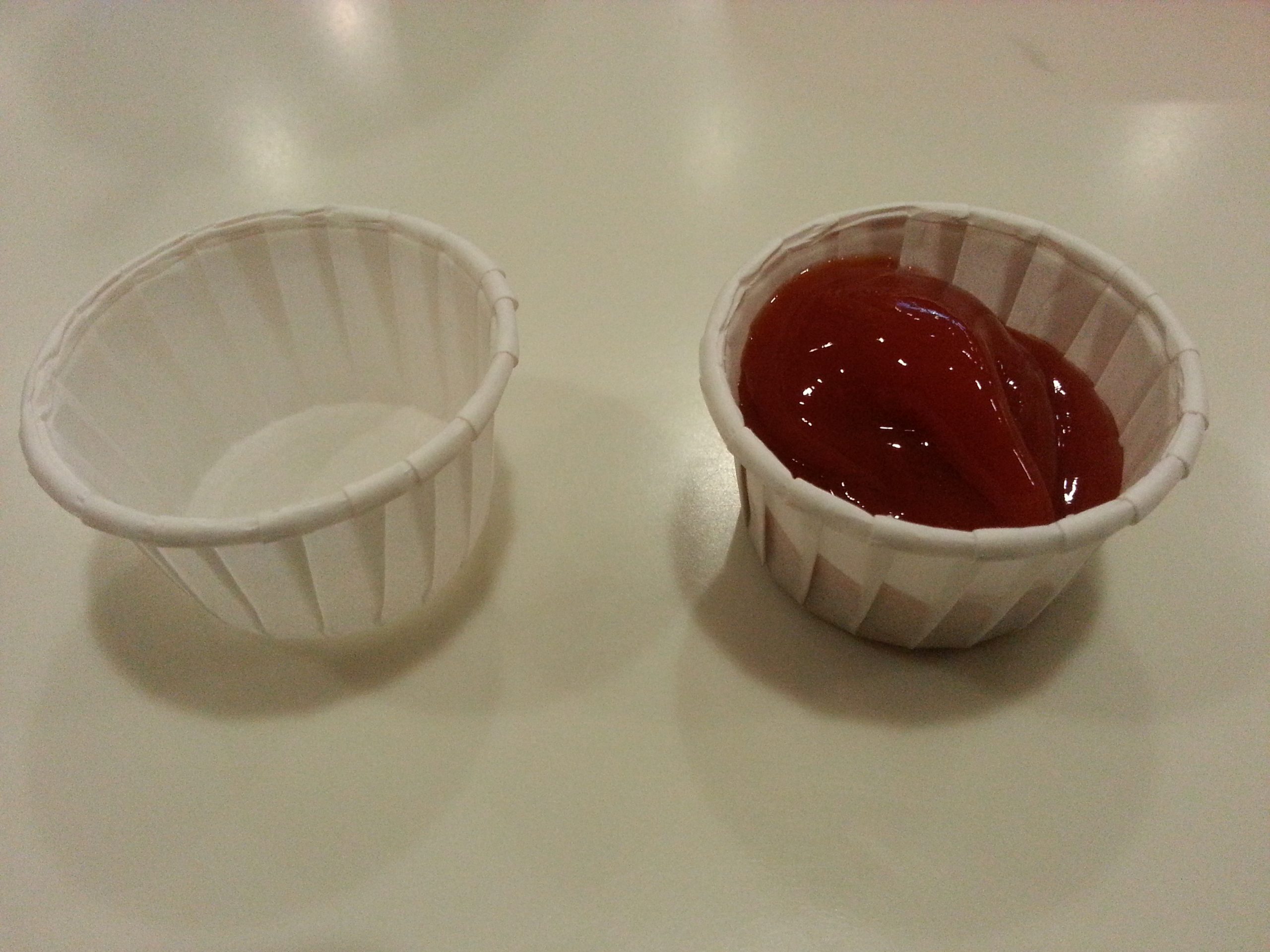 Standard empty ketchup condiment container on left juxtaposed with same container full of ketchup on the right hand side.