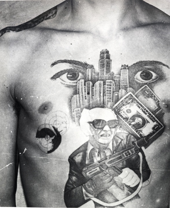 The dollar bills, skyscrapers and machine gun with the initials 'US' stamped on it convey this inmate's love for the American mafia-like lifestyle. The eyes signify 'I'm watching over you' (the other inmates in the prison or camp). The epaulette tattooed on the shoulder denotes the inmates 'rank' among the criminal caste.