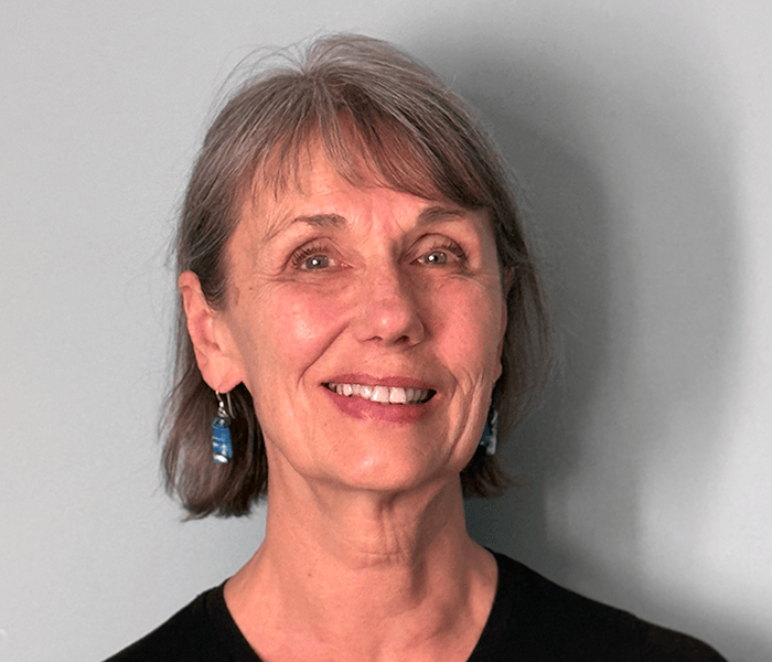Smiling middle-aged woman with short gray hair and blue earrings against a gray background.