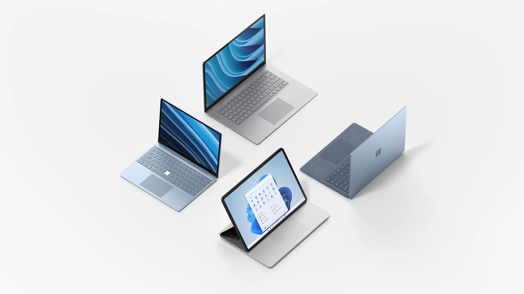 Four sleek Microsoft Surface laptops in different colors and positions are arranged on a white surface, showcasing their keyboards, screens, and modern designs. One laptop displays the Windows 11 start menu.