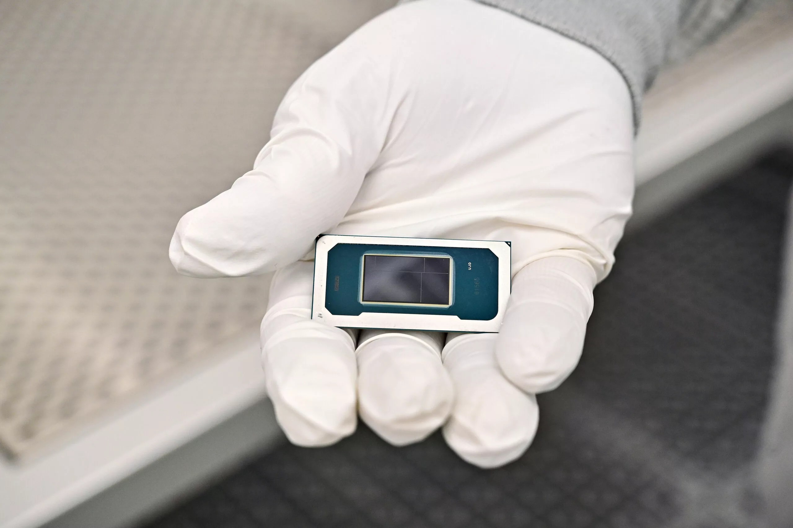 A gloved hand holds a small rectangular electronic device with a screen, possibly an 18A-enabled medical or laboratory instrument, against a blurred background.