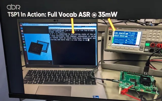 A demonstration setup shows a laptop running speech recognition software by Applied Brain Research, a microchip image on screen, an electronic testing device, and a connected circuit board labeled “TSP1 In Action: Full Vocab ASR @ 35mW.”.