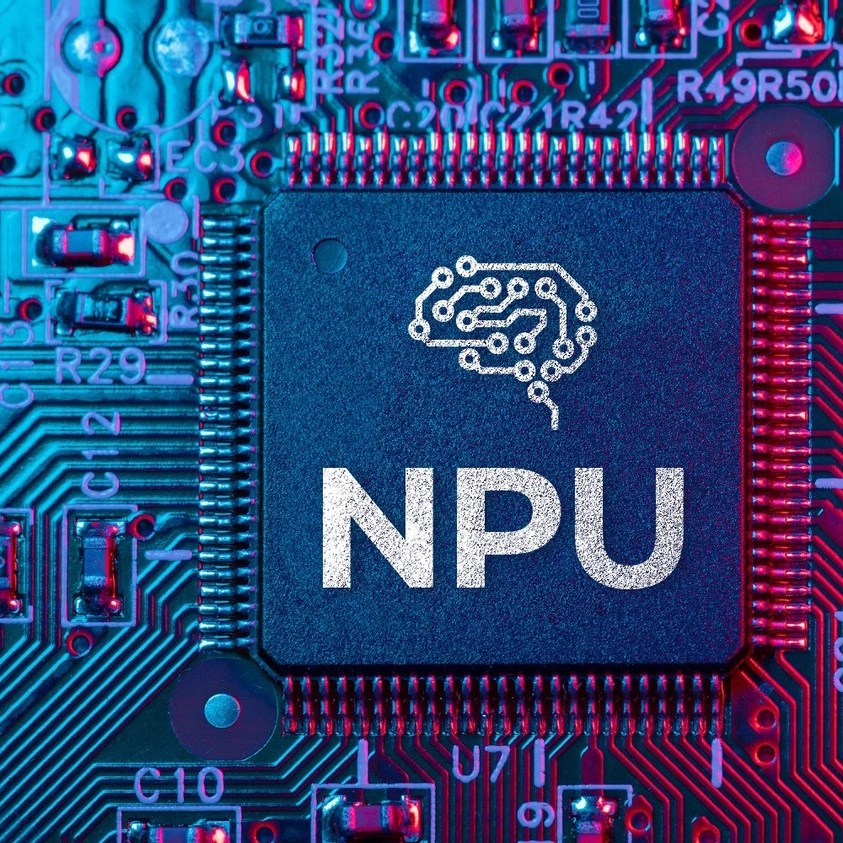 Close-up of a computer chip labeled NPU with a brain-shaped circuit design, mounted on an AI PC motherboard alongside visible electronic components.