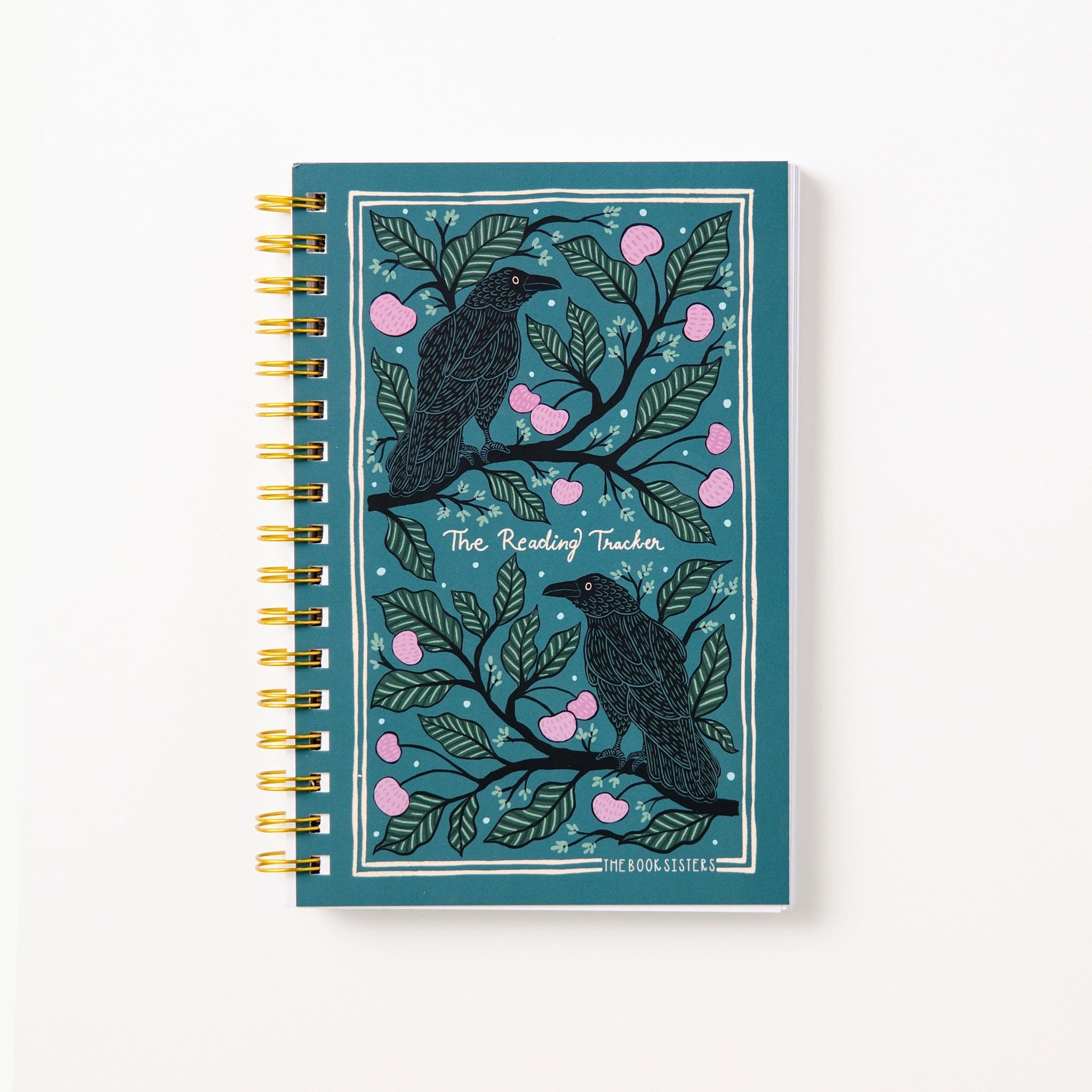 The Reading Tracker spiral notebook in teal with raven illustrations and pink fruit branches, gold wire binding, by The Book Sisters