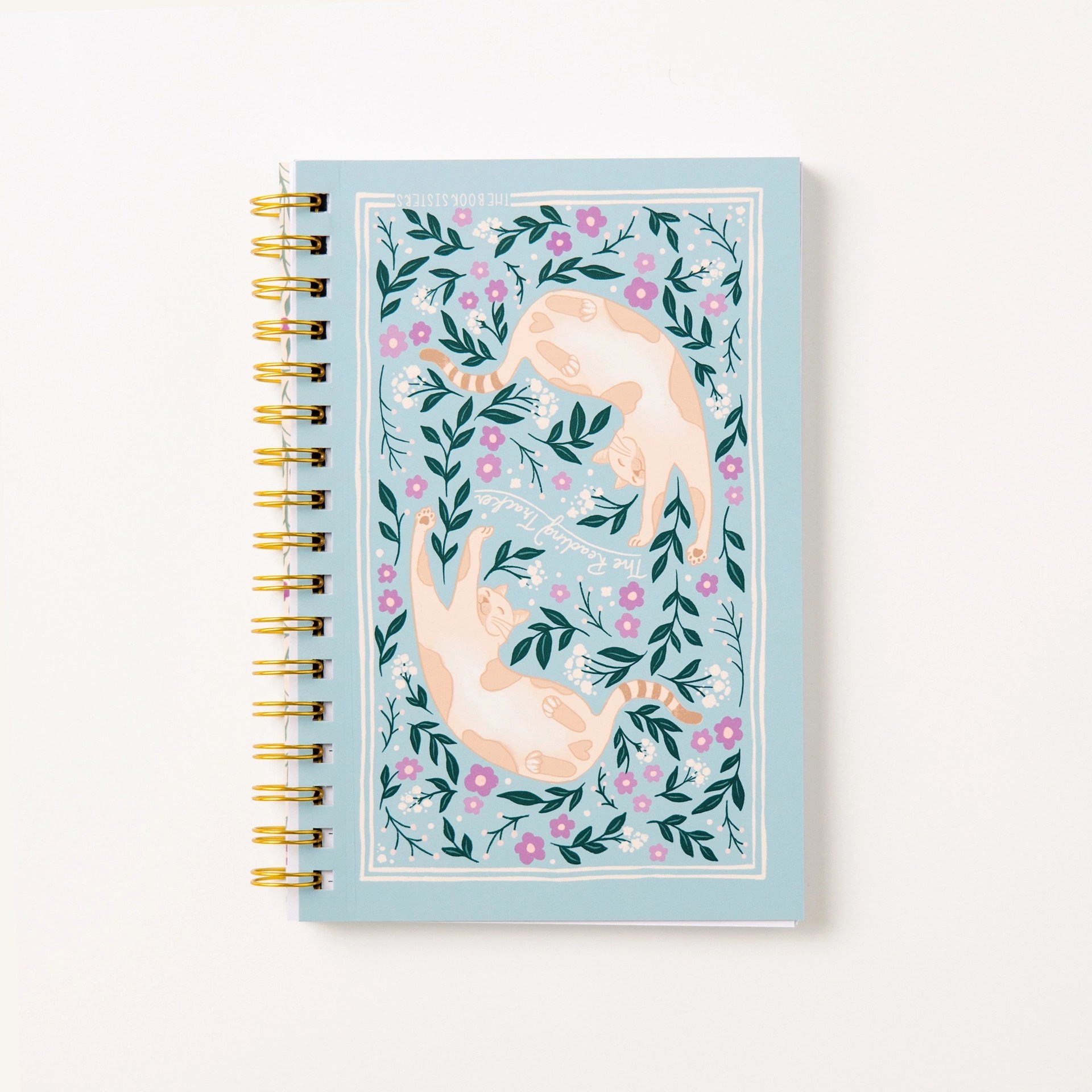 The Reading Tracker spiral notebook in light blue with playful cat illustrations and purple flowers, gold wire binding, by The Book Sisters