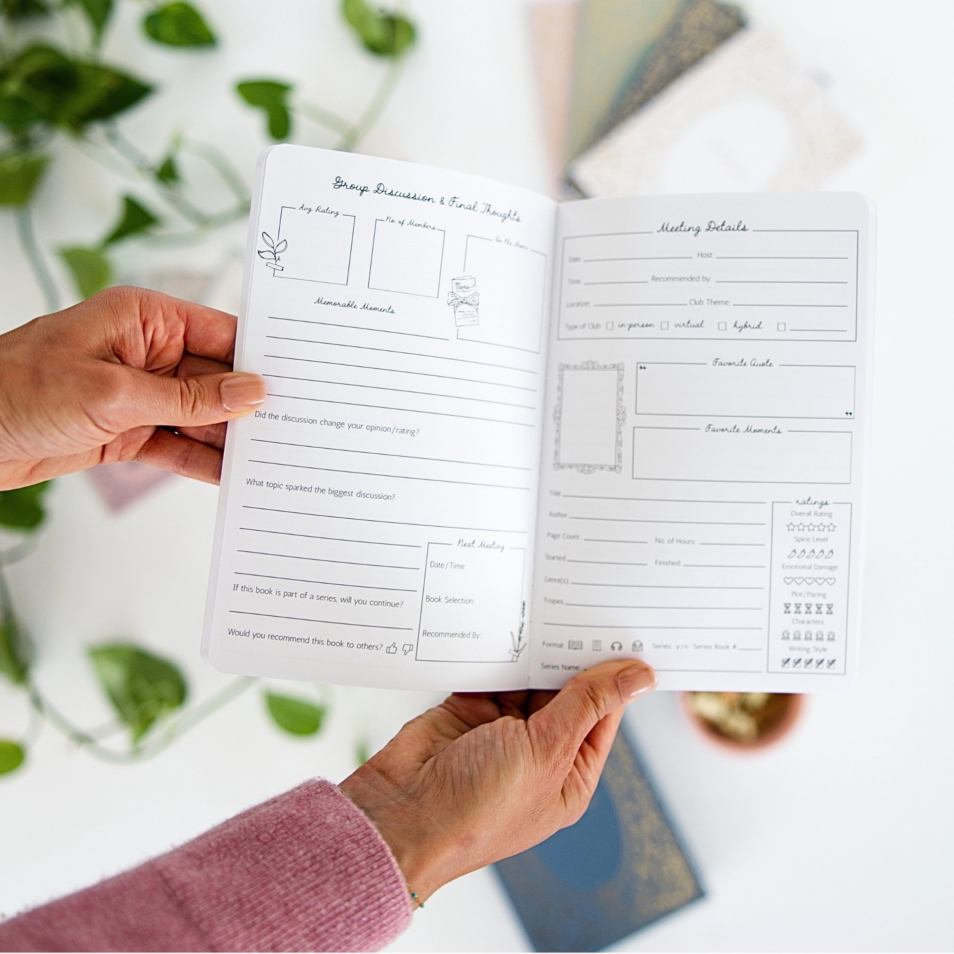 Hands holding open My Book Club journal to the Group Discussion and Meeting Details pages on a cozy tabletop.