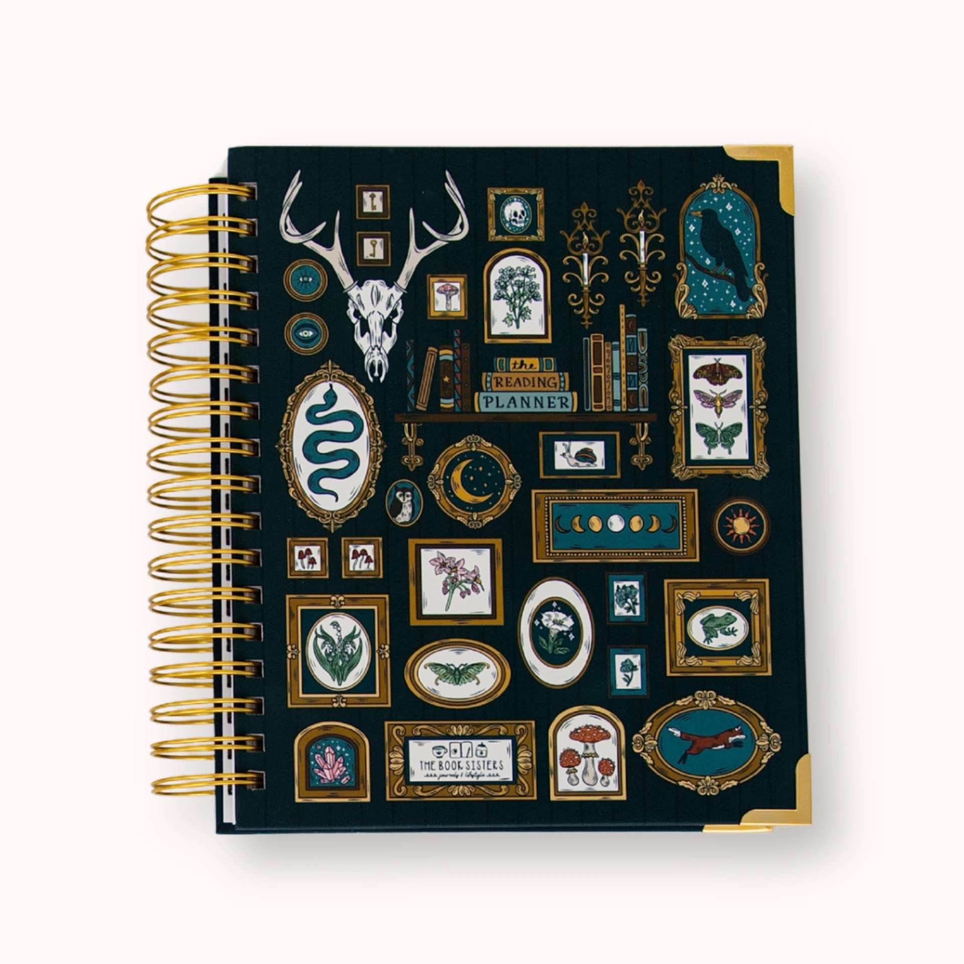 Dark teal hardcover reading planner with gold wire binding, illustrated with a gothic gallery wall of a deer skull, moon phases, a raven, snake, and mushrooms around a bookshelf reading "The Reading Planner"