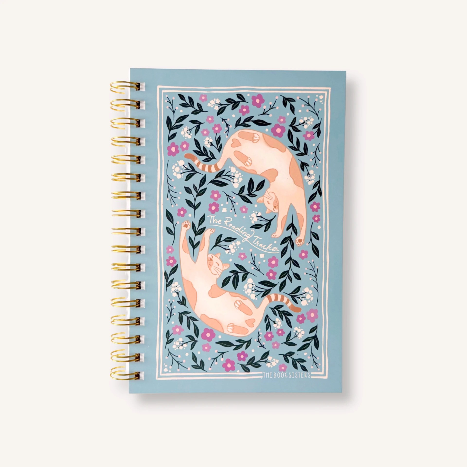 The Reading Tracker spiral notebook in light blue with playful cat illustrations and purple flowers, gold wire binding, by The Book Sisters