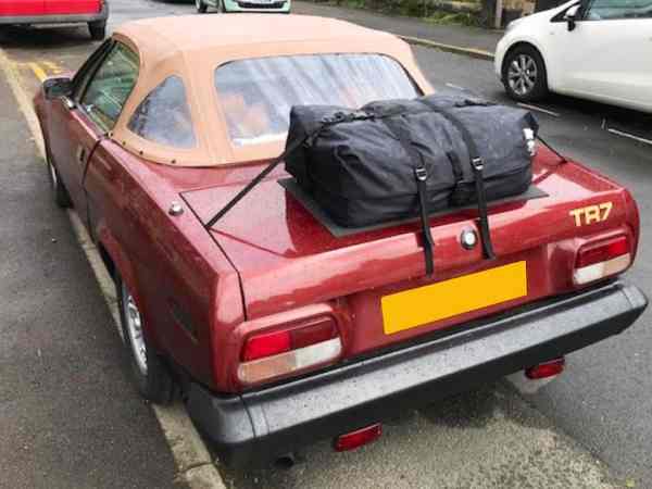 side view of a burgundy triumph tr7 convertible with a biege hood and a boot-bag luggage rack fitted to the boot/trunk