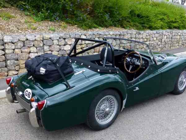 green triumph tr3 with a boot-bag original luggage rack fitted next to a stone wall 