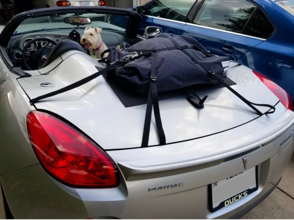 silver pontiac solstice on a drive hood down with a terrier in the car and a luggage rack fitted