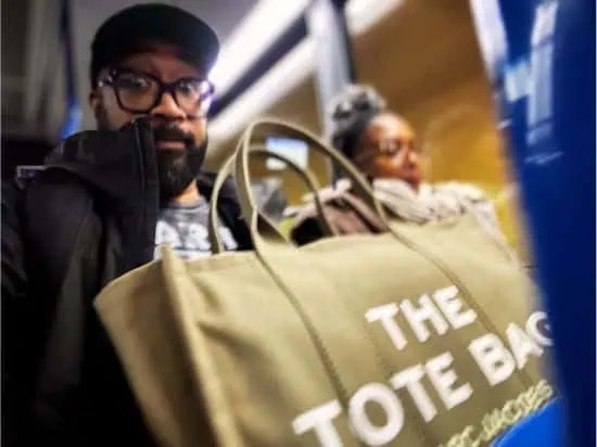 Two savvy entrepreneurs are riding the bus, each strategically planning their next business move. One rocks a stylish "The Tote Bag," designed to be the ultimate organizer for ambitious go-getters. This bag is a powerhouse accessory—perfect for storing insightful tips for busy entrepreneurs always on the move. - Boss Uncaged™ OmniMedia Inc.