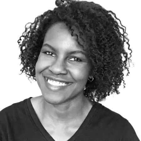 Confident woman with curly hair smiles directly at camera in dark top and hoop earrings, standing against crisp white background. - Boss Uncaged™ OmniMedia Inc.
