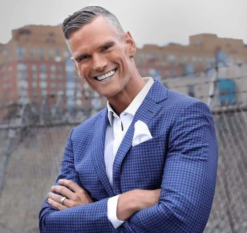 Markus Kaulius, Chief Culture Officer, exudes confidence outdoors in a blue checkered suit, arms crossed, smiling, urban backdrop. - Boss Uncaged™ OmniMedia Inc.