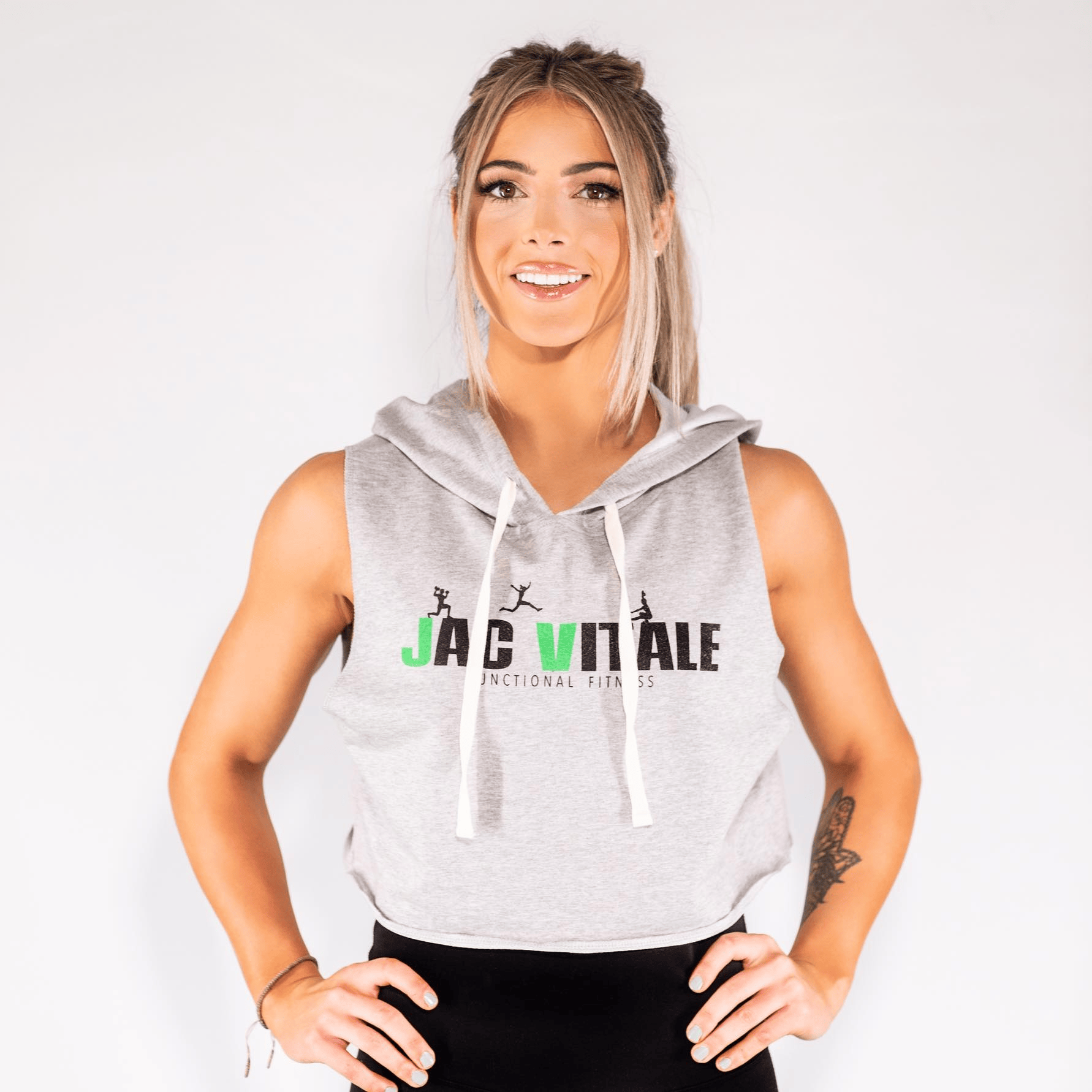 Confident blonde woman in JAC VITALE Functional Fitness hoodie, hands on hips, stands strong and smiling against a white background. - Boss Uncaged™ OmniMedia Inc.