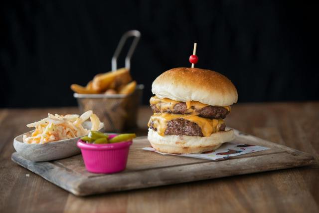 Mouthwatering cheeseburger served with fries and coleslaw on a wooden board.