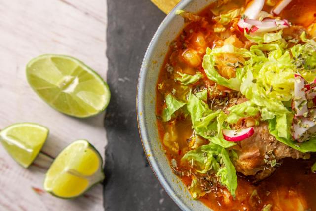 Close-up of a vibrant Mexican pozole in a bowl with fresh lime slices.