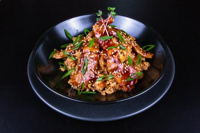 Delicious spicy pork stir-fry with vibrant vegetables and sesame seeds on rice, perfect for a savory meal.