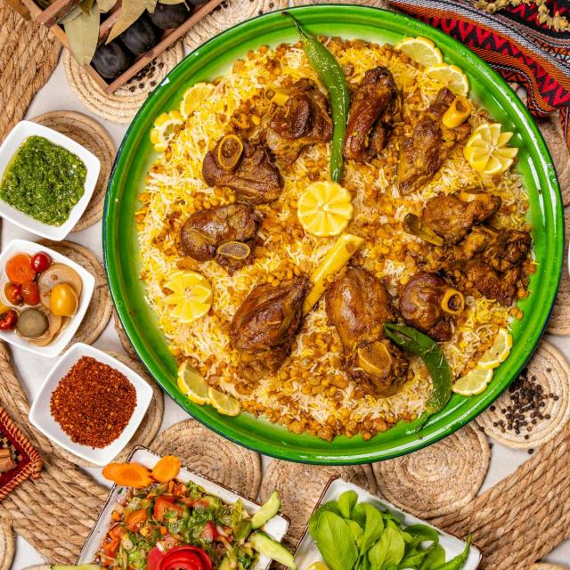Top view of a flavorful lamb rice dish with spices, herbs, and lemon garnishes.