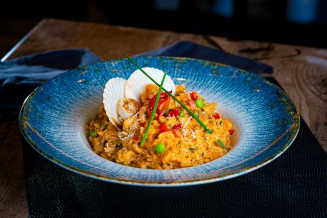 Delicious seafood risotto topped with scallops, served in a blue ceramic dish.