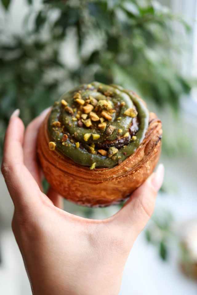 Delicious pistachio-topped cinnamon bun held outdoors, showcasing texture.