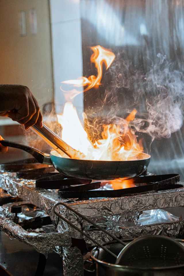 Close-up of chef's hand sautéing with intense flames in a professional kitchen setting.