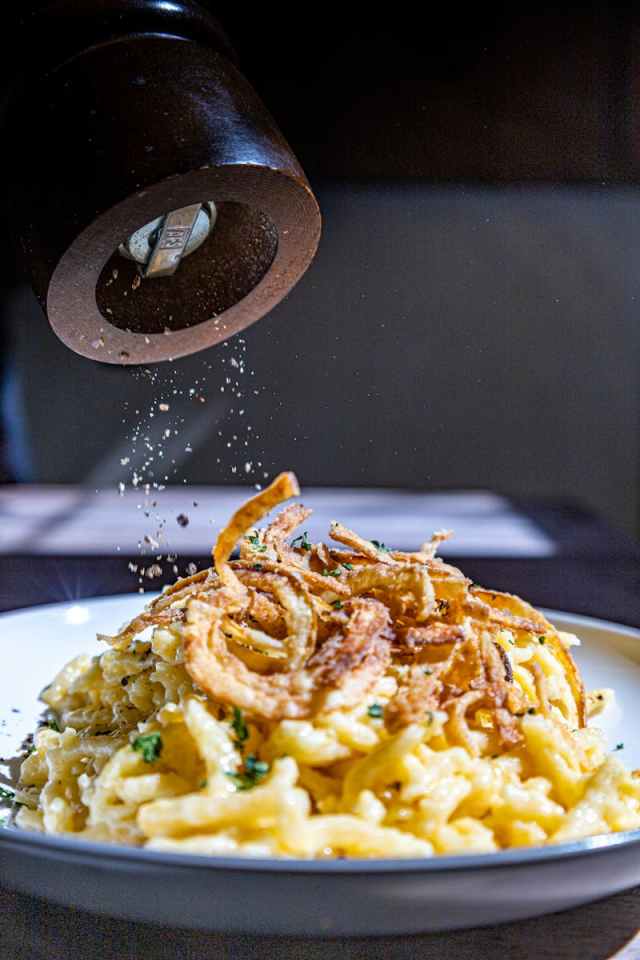 Close-up of a plate of pasta topped with crispy onions and grated cheese, seasoned with pepper.