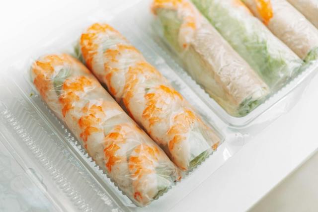 Close-up of freshly prepared Vietnamese spring rolls packaged in clear plastic containers.