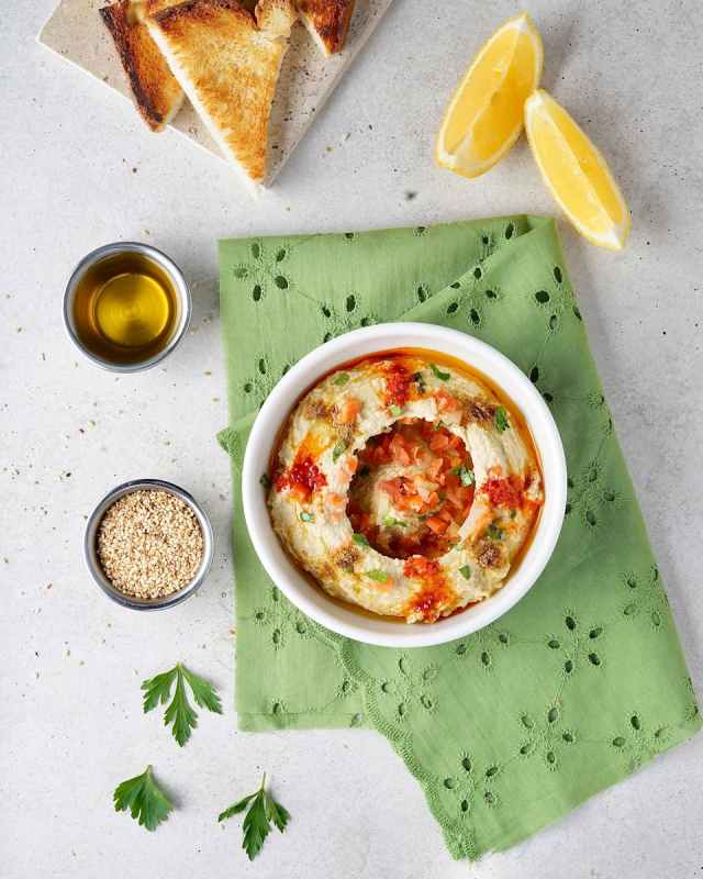 Appetizing hummus dish with garnishes, toast, and sesame seeds in a bright, inviting setting.