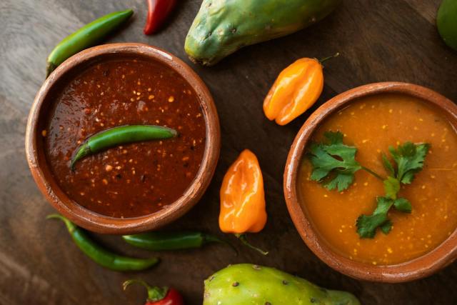 Top-down view of spicy Mexican salsas with peppers and fresh ingredients on a wooden table.