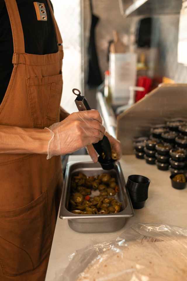 Chef wearing an apron prepares jalapeno peppers in a commercial kitchen setup.