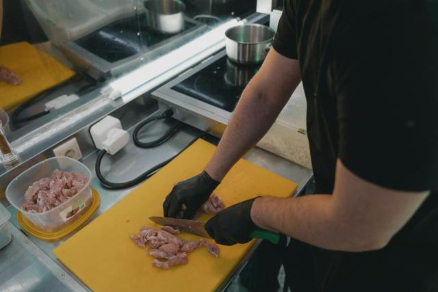 Man slicing raw meat on a yellow cutting board in a modern kitchen setting.