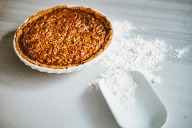 Close-up of a freshly baked pecan pie with scattered flour on a marble surface, inviting dessert lovers.