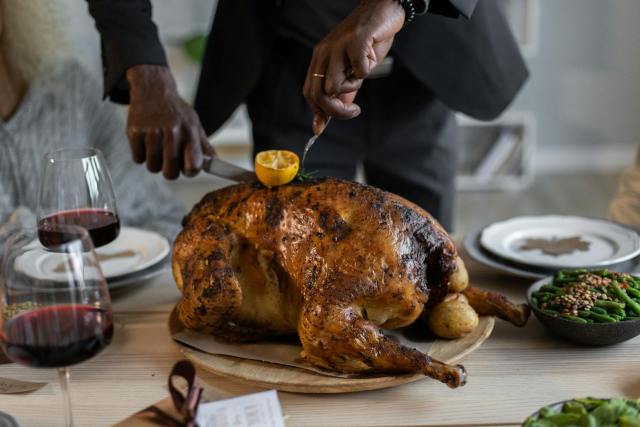 Crop anonymous African American male in suit cutting piece of roasted turkey with knife and fork while having Thanksgiving dinner
