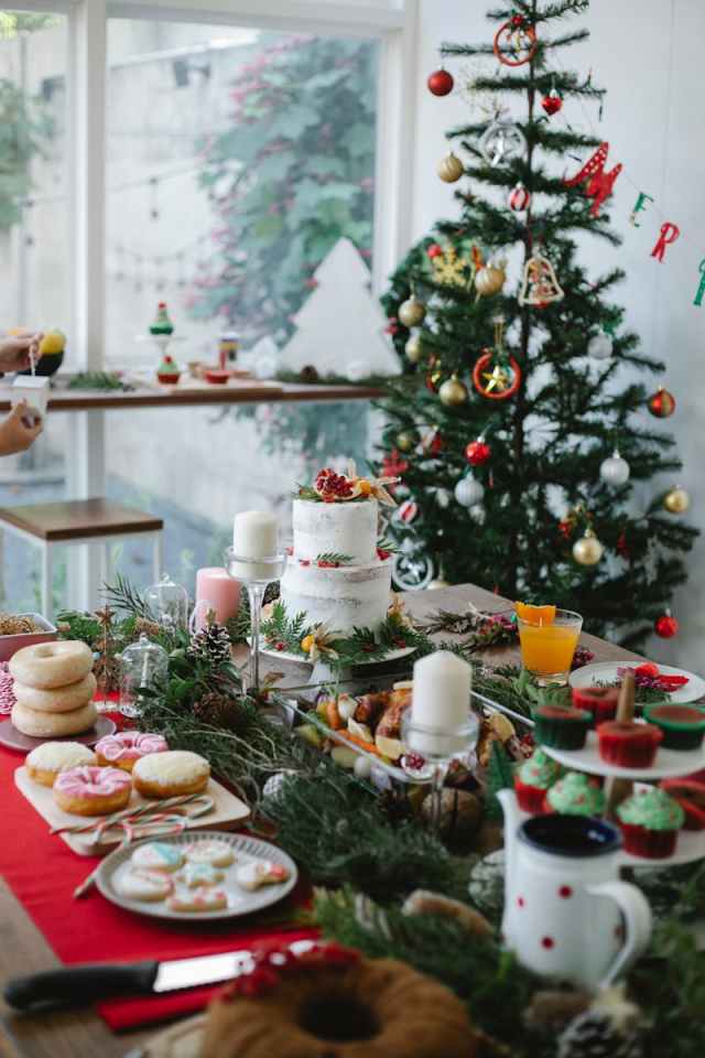 A beautifully decorated Christmas table with cakes and desserts, set indoors near a Christmas tree.