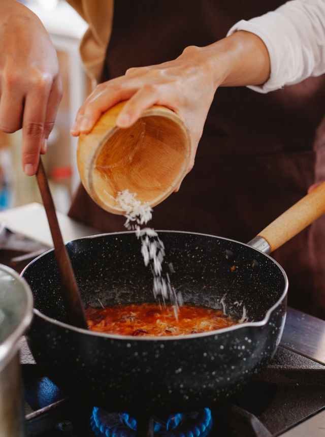 Close-up of cheese being added to simmering tomato sauce on a stovetop.