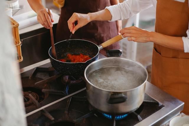 Close-up of two women cooking; stirring sauce and boiling water on stove.