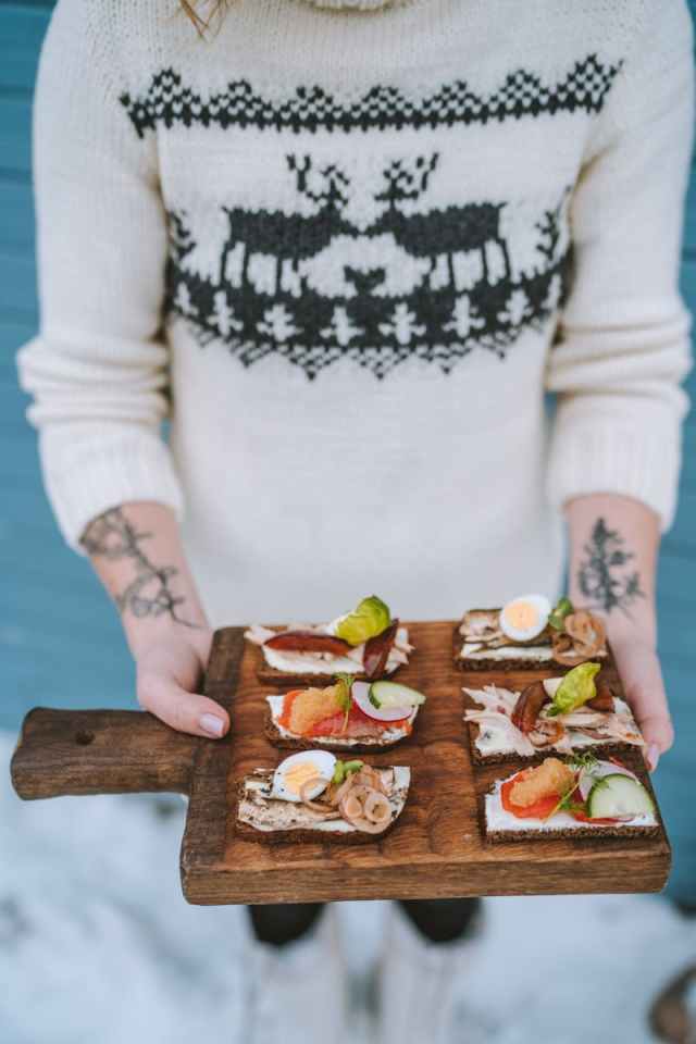 Person in winter sweater holding a tray of festive open-faced sandwiches.