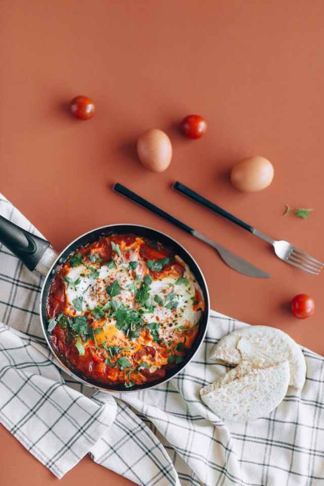 Tasty shakshuka with eggs garnished with parsley, served with pita and fresh ingredients.