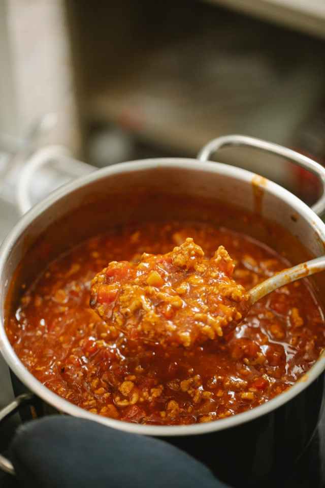High angle freshly cooked yummy bolognese sauce in spoon and saucepan placed on stove in kitchen