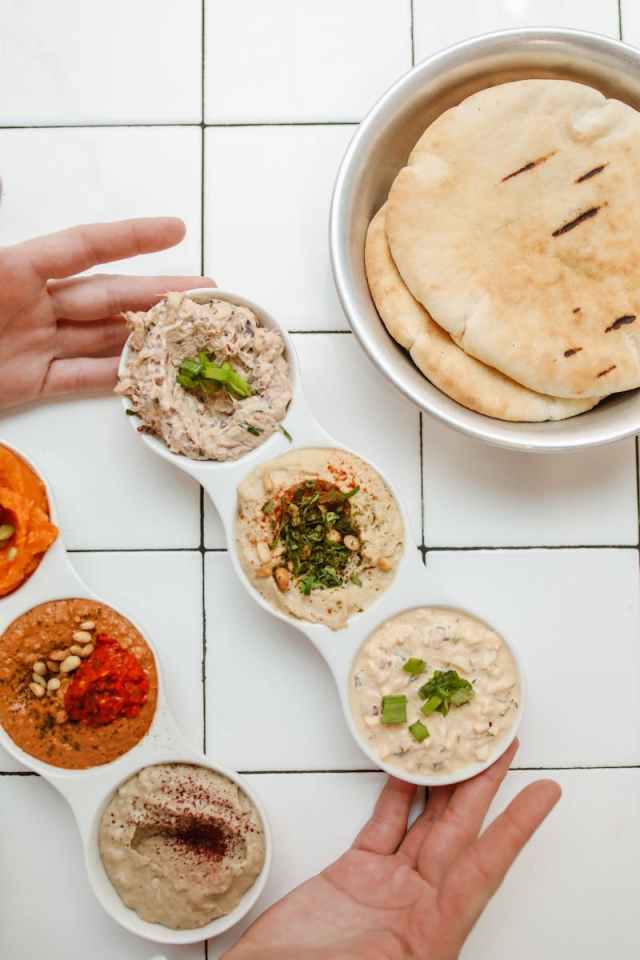 Colorful assortment of Middle Eastern dips with pita bread on a white tiled surface.