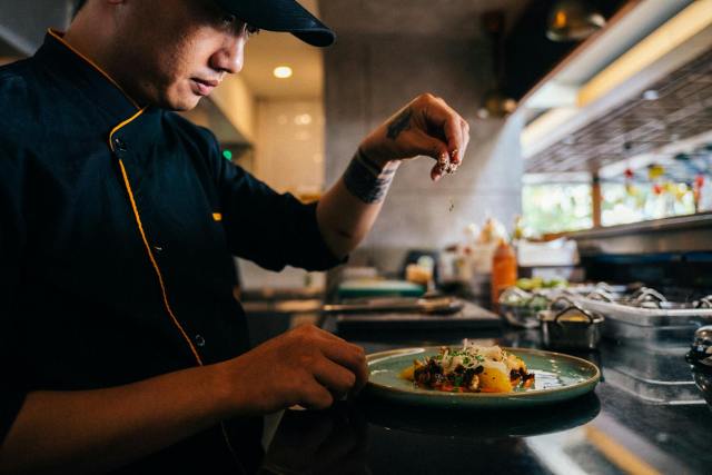 Chef skillfully sprinkles seasoning on a beautifully presented gourmet dish in a professional kitchen.