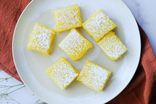Top-down view of lemon bars dusted with powdered sugar on a round plate.