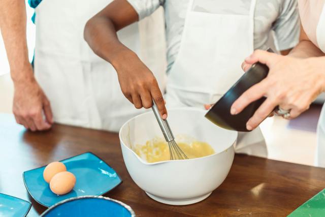 A close-up of hands whisking batter in a bowl, showcasing teamwork in cooking.