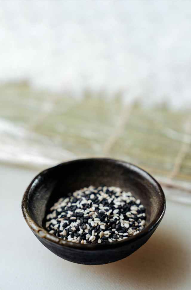Aesthetic close-up of black and white sesame seeds in a ceramic bowl on a textured surface.