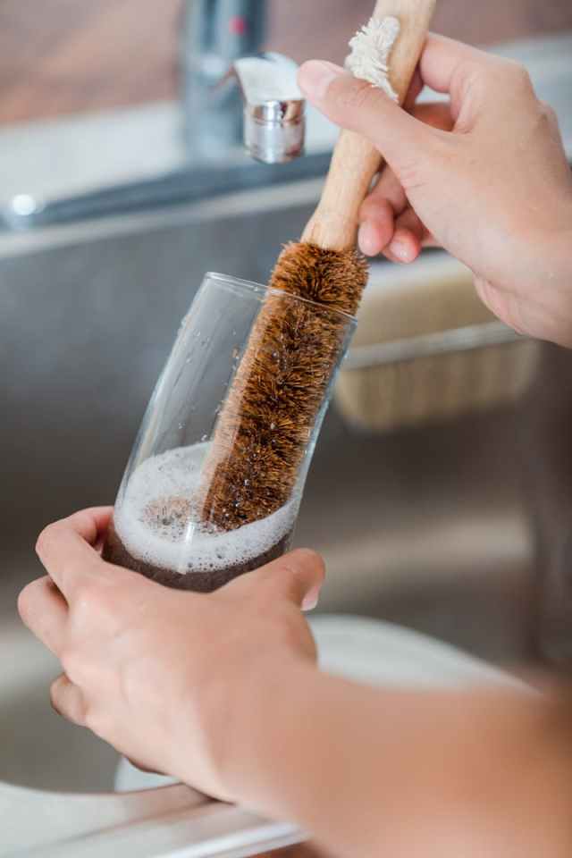 Detailed view of hands cleaning a glass with a brush at a sink.