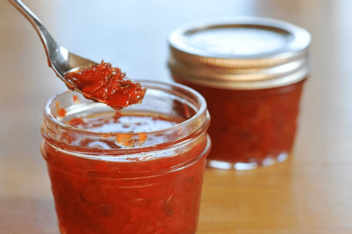Glass jar of strawberry pepper jelly with a spoon scooping it up.
