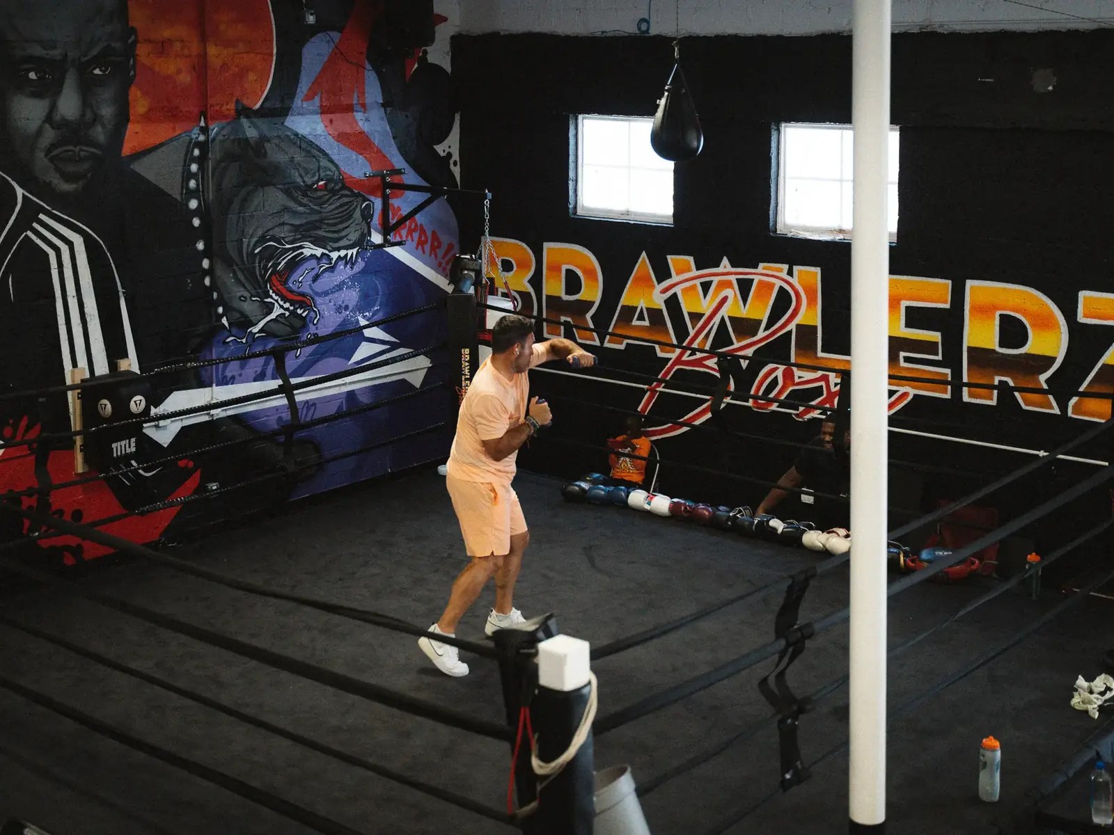 Fighter shadowboxing in the Brawlerz ring under the gym's sunset logo mural